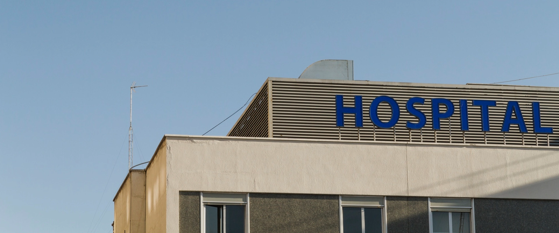 Edificio con cartel que dice "HOSPITAL" en letras azules sobre fondo claro, con cielo despejado.