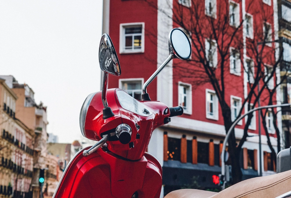 Motocicleta roja estacionada frente a edificio rojo con ventanas blancas en un entorno urbano.