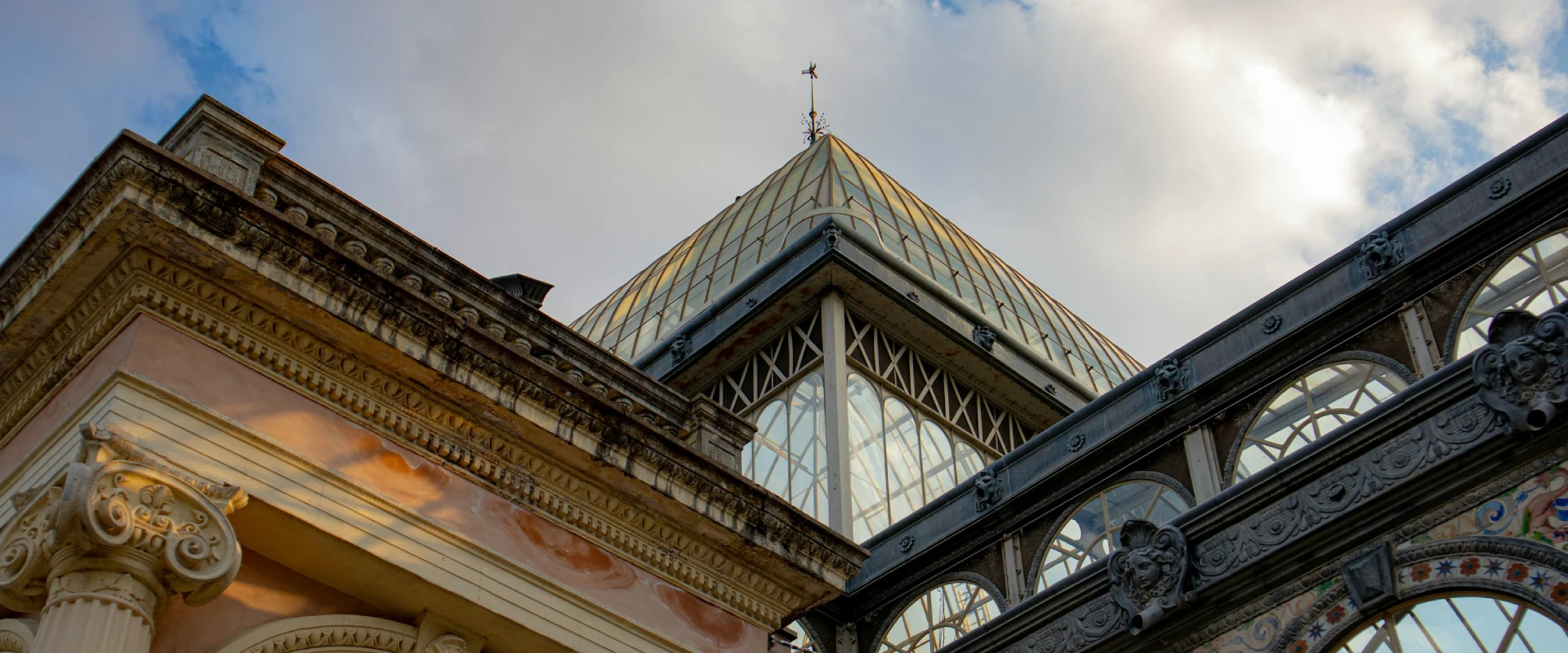Techo de vidrio y paredes decoradas de un edificio histórico, con cielo nublado en el fondo.