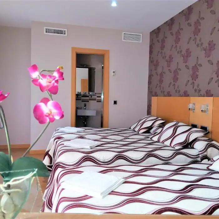 Habitación de hotel con dos camas, decoración floral y una puerta abierta al baño.