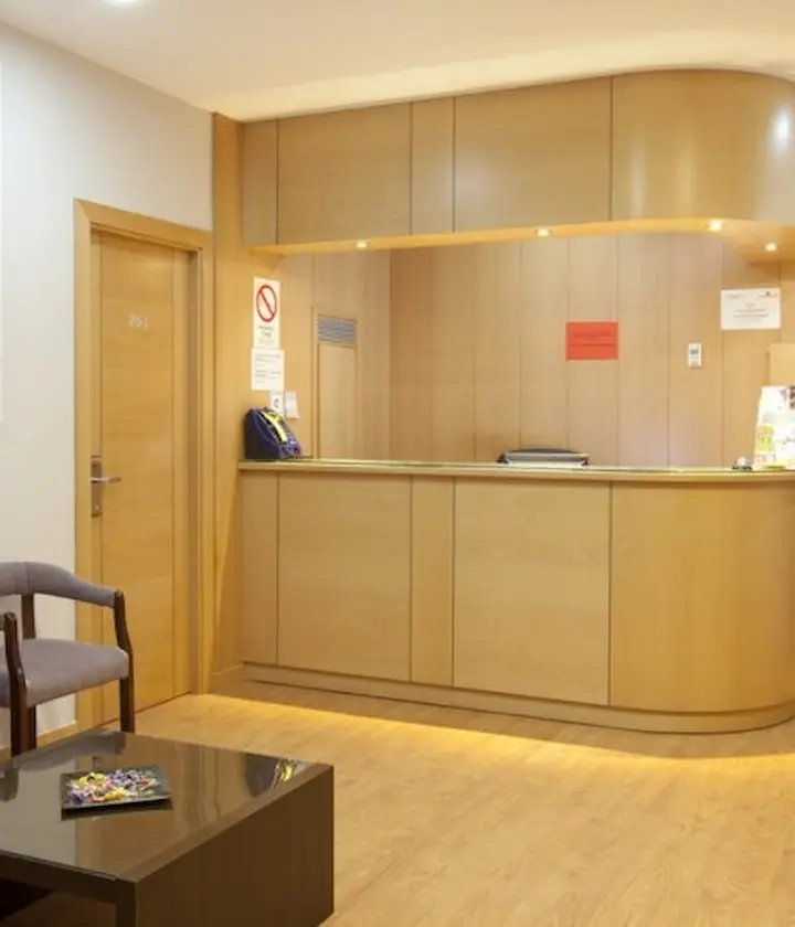 Recepción de madera clara en una oficina o clínica, con mesa y sillas en la sala de espera.