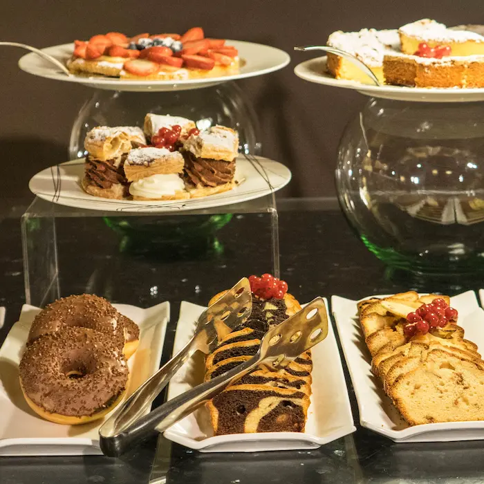 Bandejas con donas, pasteles y fruta en un buffet de postres.