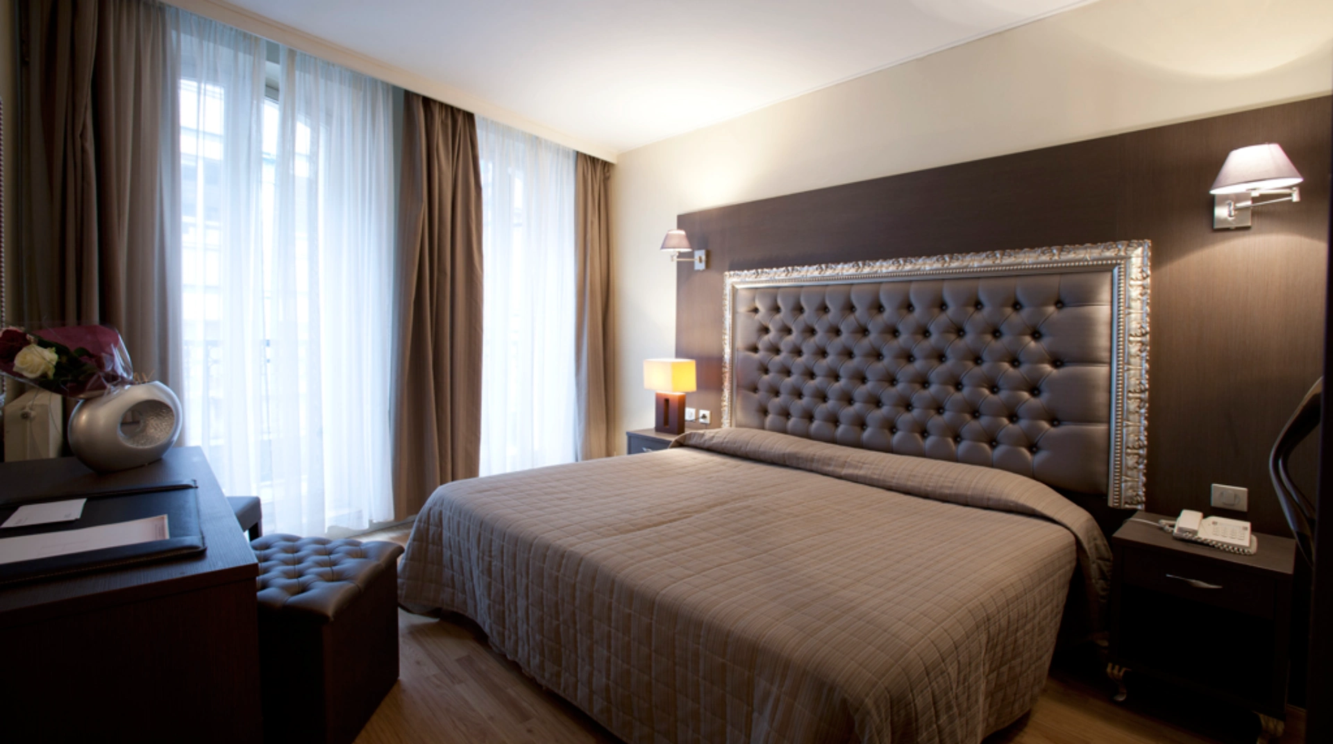 Chambre d'hôtel élégante avec grand lit, tentures beiges et lumière douce.