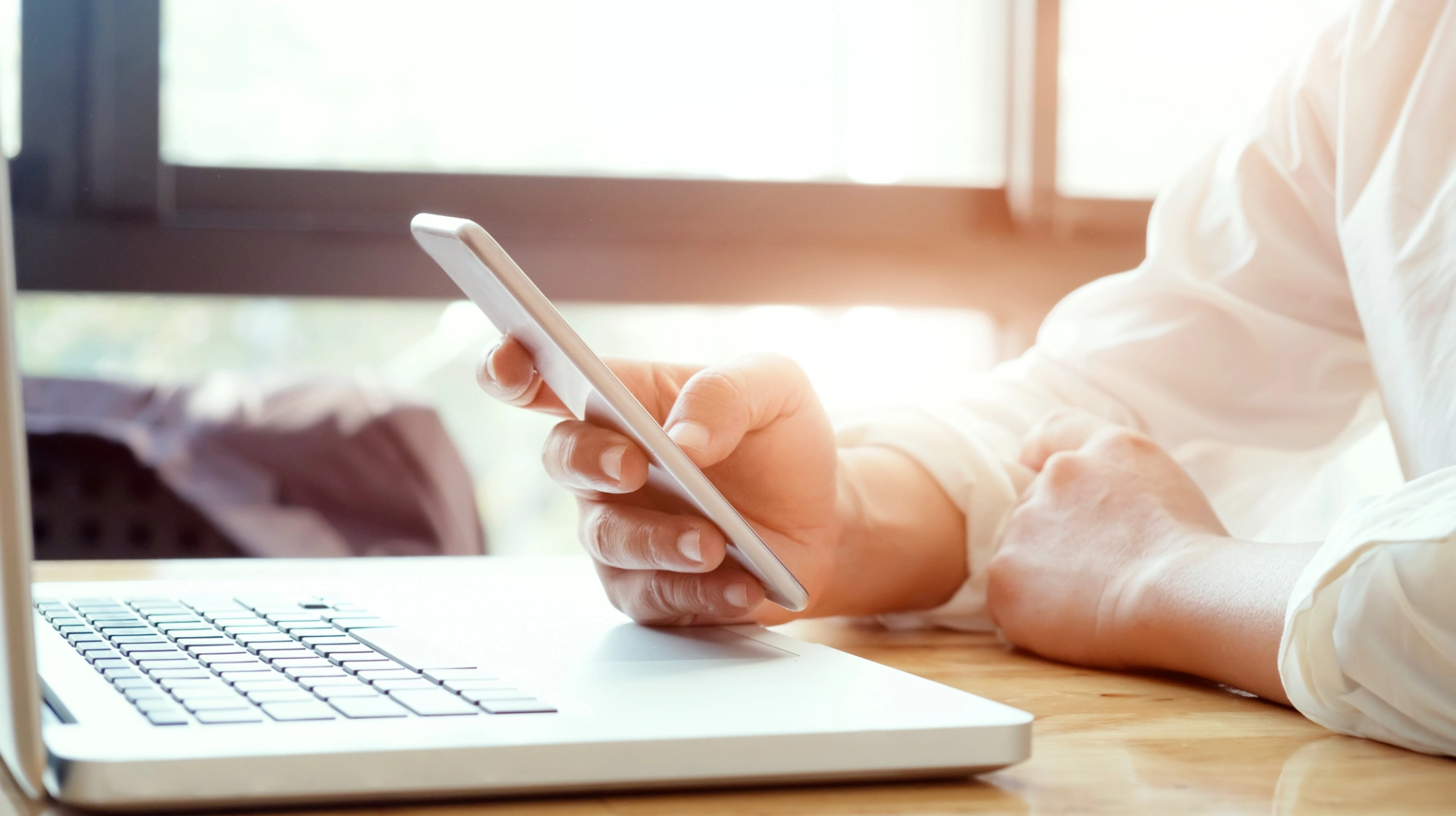 Personne utilisant un smartphone devant un ordinateur portable sur une table en bois.