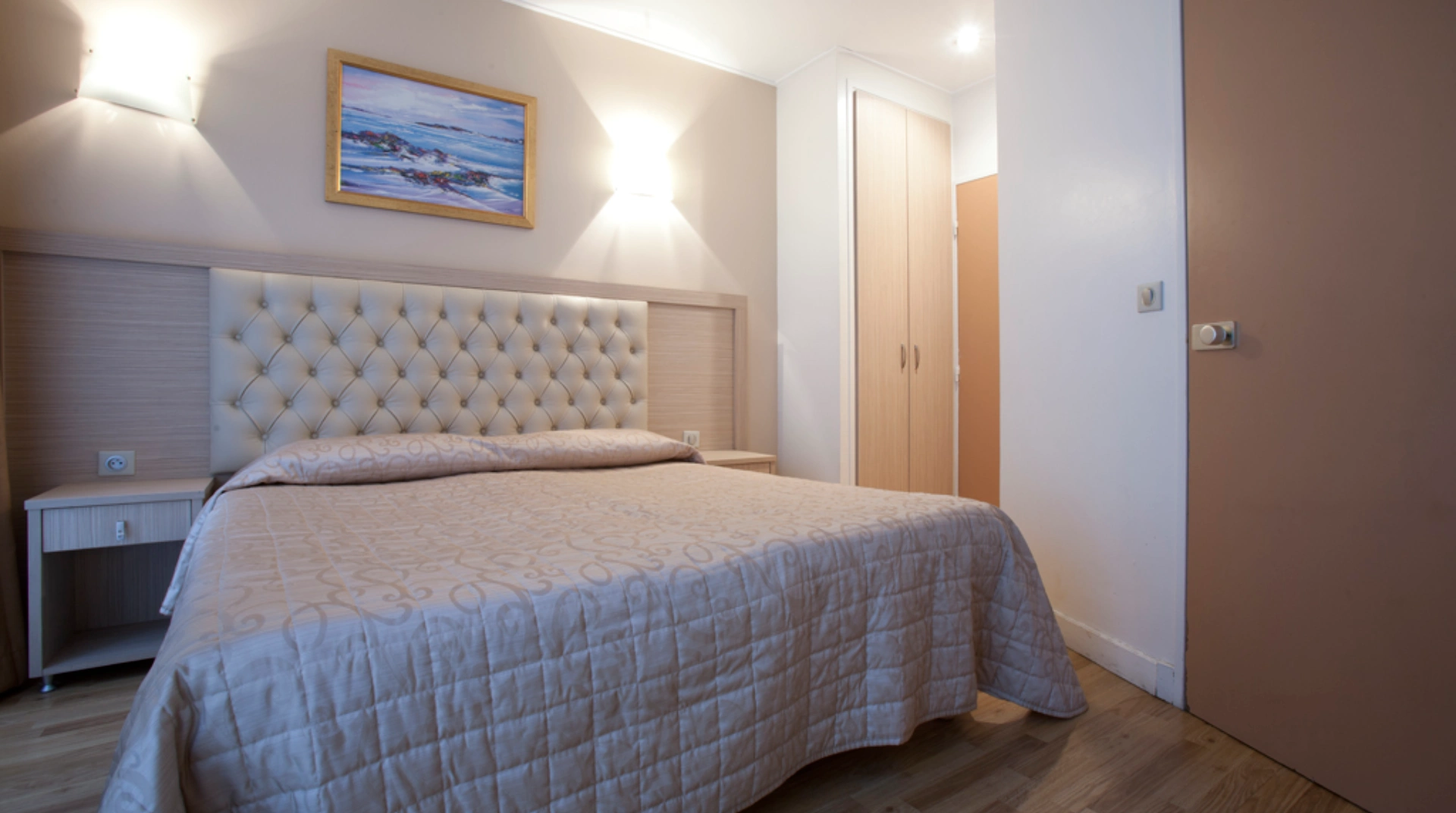 Chambre avec lit double, tableau mural et lumière tamisée.
