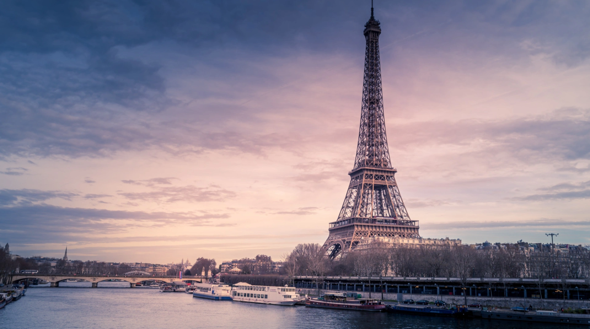 Tour Eiffel au coucher du soleil, vue depuis la Seine avec des bateaux.