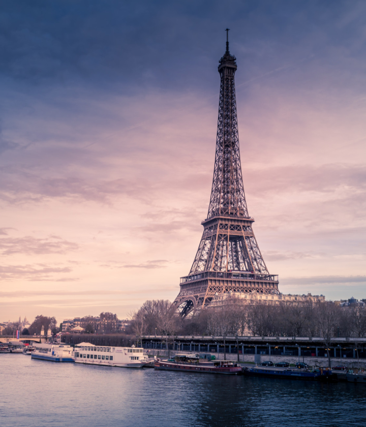 Tour Eiffel au crépuscule avec bateaux sur la Seine, ciel rose et violet en arrière-plan.