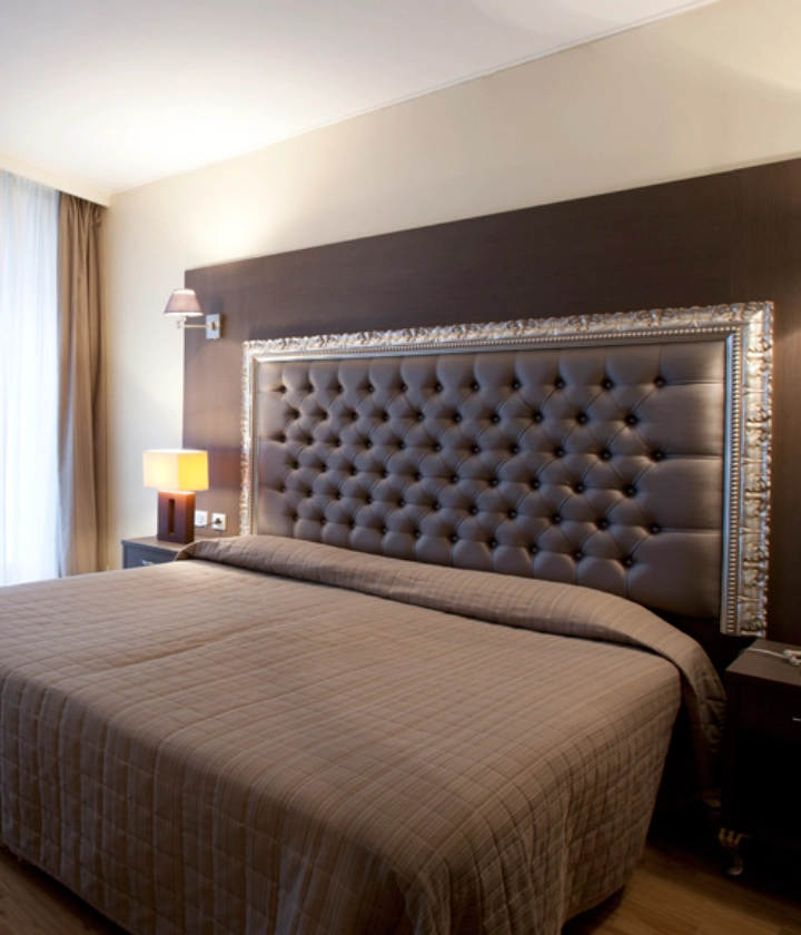 Chambre d'hôtel élégante avec lit double, tête de lit capitonnée et lampes de chevet.