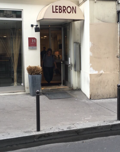 Entrée d'un bâtiment avec store "LEBRON", une personne sort par la porte ouverte.