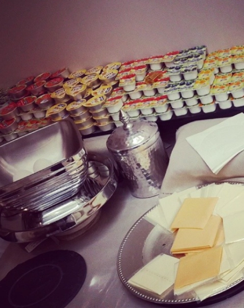 Boîtes de crème empilées, assiettes métalliques et tranches de fromage sur une table.
