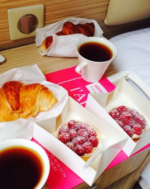 Croissants, tartes aux framboises et café sur une table en bois.