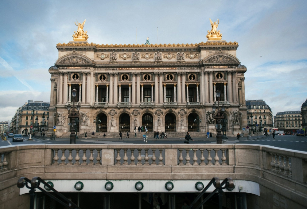 Façade d'un bâtiment historique avec statues dorées et colonnes, ciel bleu en arrière-plan.