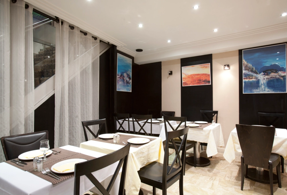 Salle de restaurant élégante avec des tables dressées et des œuvres d'art aux murs.