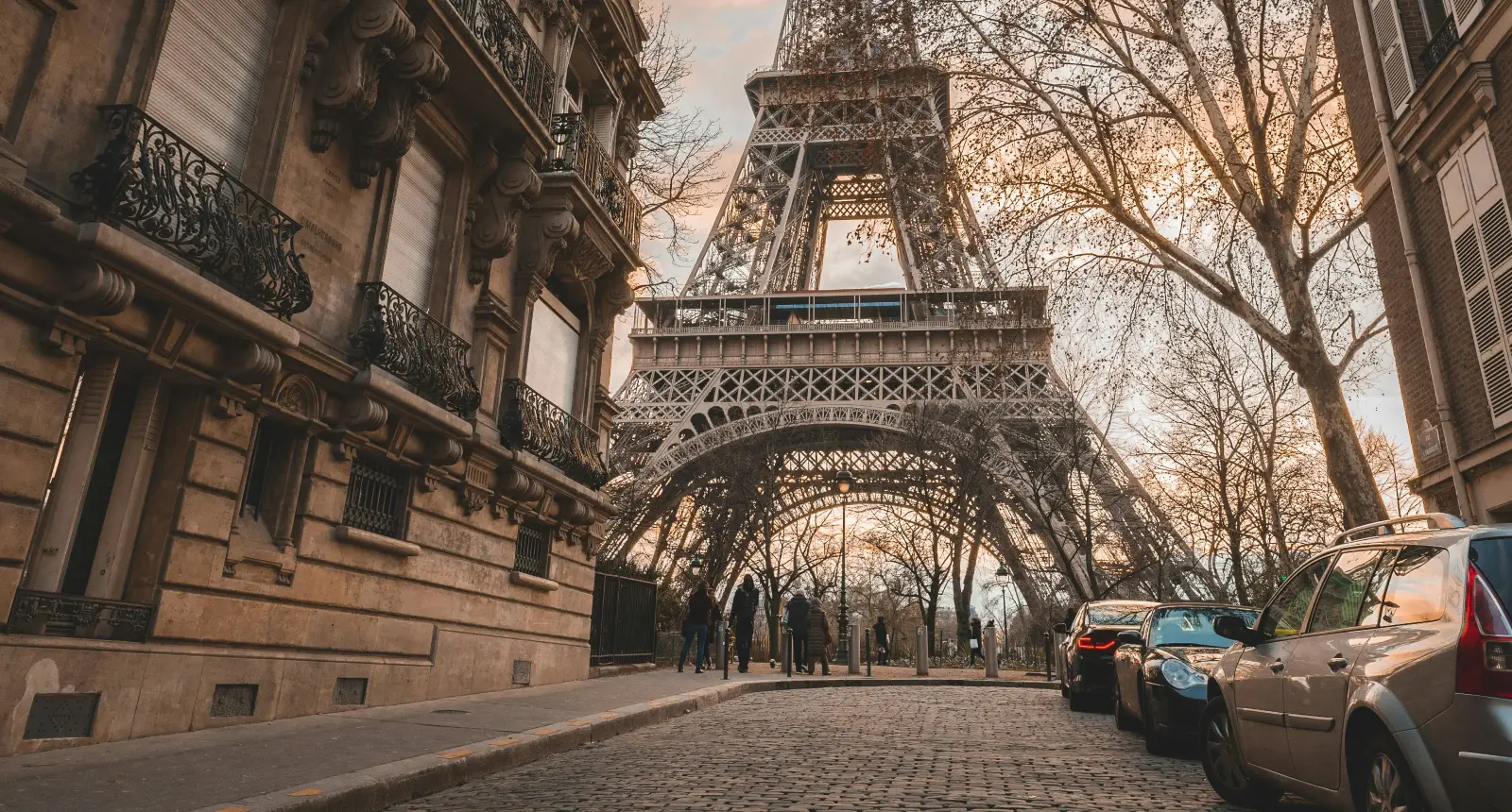 Vue de la Tour Eiffel depuis une rue pavée avec voitures et bâtiments anciens.