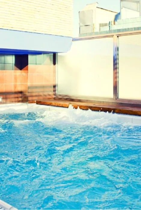 Piscina con agua azul y espuma cerca de muros de azulejo y vidrio iluminados por el sol.