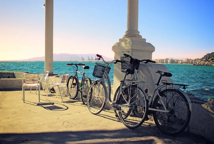 Bicicletas estacionadas junto al mar, cerca de sillas, en un día soleado.