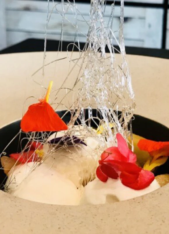 Postre adornado con flores comestibles y caramelo hilado en un plato sofisticado.