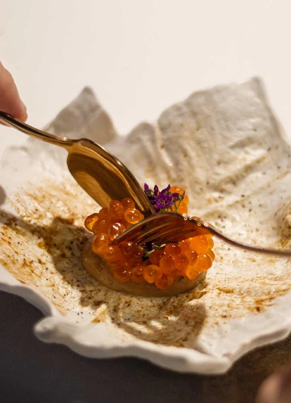 Un plato elegante con caviar naranja y flores pequeñas, servido sobre un fondo con textura única.