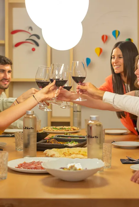 Personas brindando con copas de vino en una mesa con comida y decoración colorida.