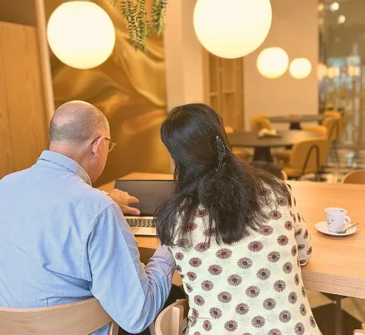 Una pareja sentada en un café, viendo una computadora portátil.