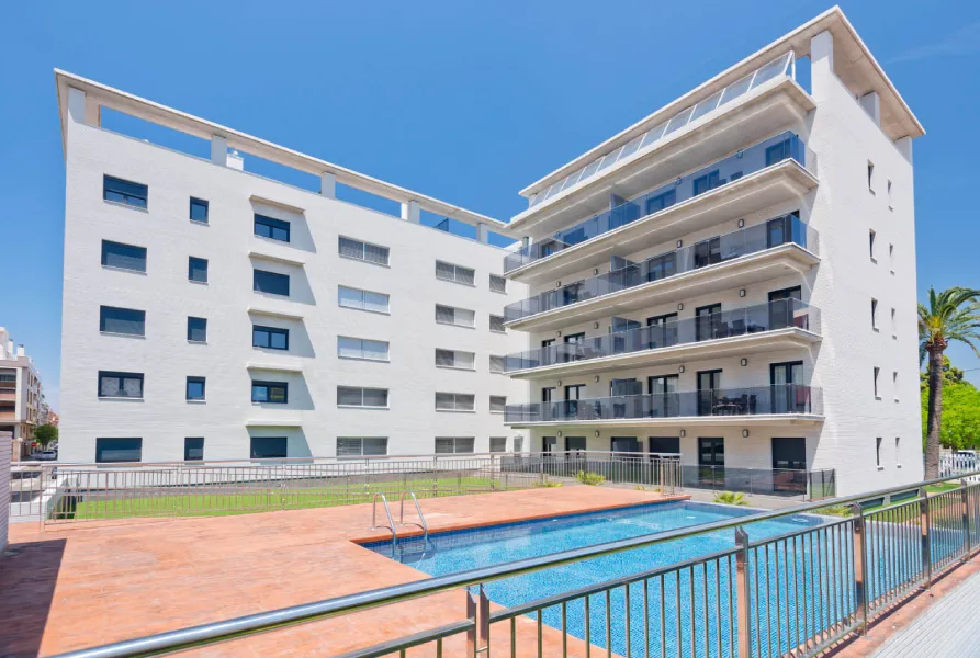 Edificio blanco moderno con piscina y balcones, cielo despejado.