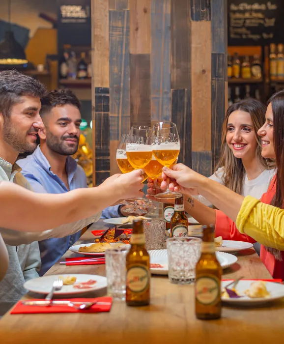 Grupo de amigos celebrando con cervezas y comida en un restaurante.