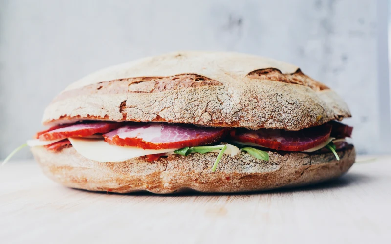 Sándwich de pan rústico relleno de jamón, queso y verduras sobre una superficie de madera.