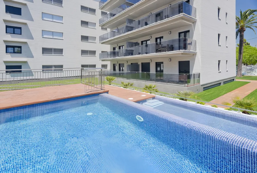 Edificio moderno con balcones y piscina frente a un césped cuidado.