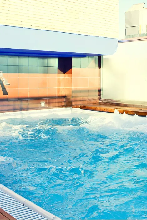 Piscina al aire libre con azulejos azules y naranja, rodeada de edificaciones.