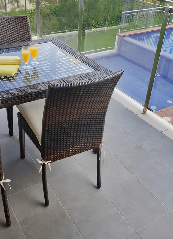 Terraza con mesa y sillas de mimbre, dos jugos y piscina al fondo.