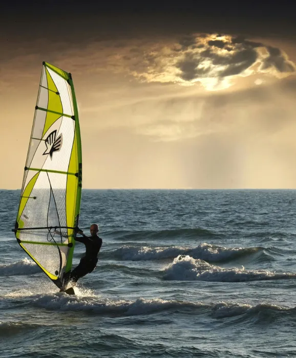 Persona haciendo windsurf al atardecer con cielo nublado y olas suaves en el mar.