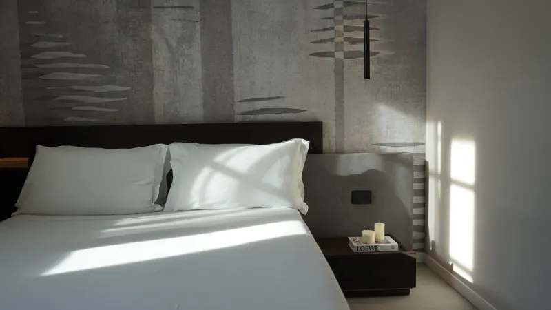 Cama moderna en habitación con luz natural y decoración minimalista.