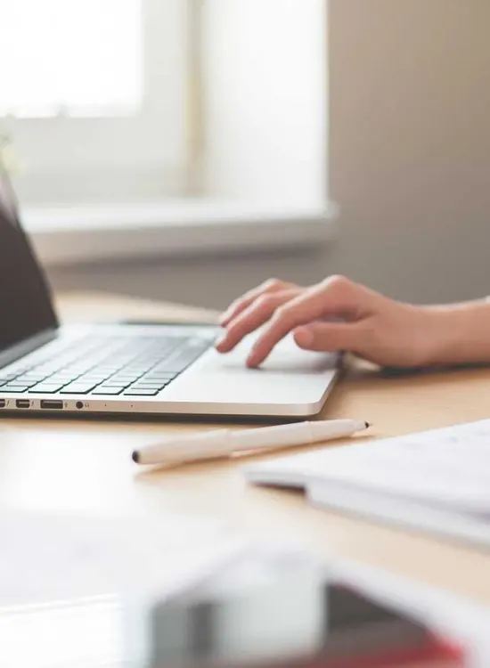 Mano usando una laptop sobre un escritorio con documentos y un bolígrafo.