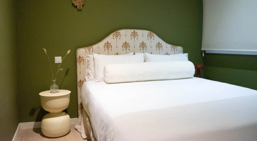 Cama doble blanca con cabecero decorado en habitaci&oacute;n verde.