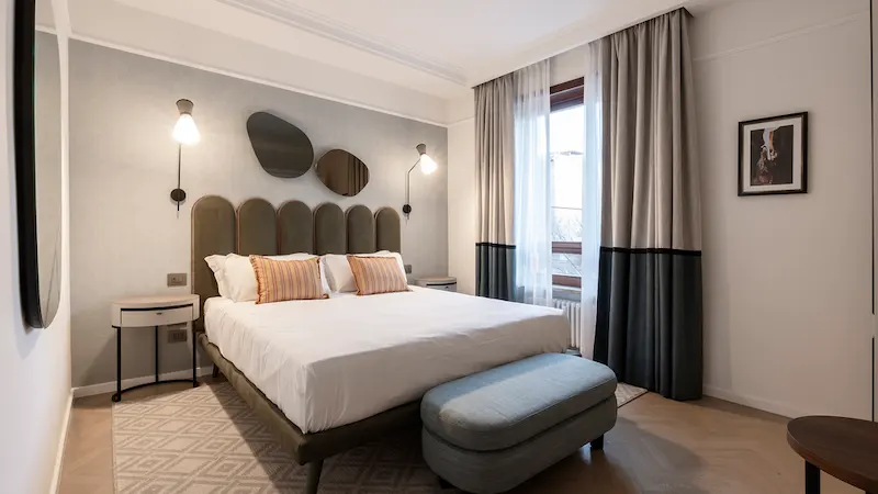 Dormitorio moderno con cama, lámparas, espejo, ventana grande y cortinas.