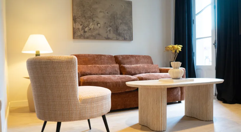 Sala de estar con sof&aacute; marr&oacute;n, butaca, mesa de madera y l&aacute;mpara encendida.