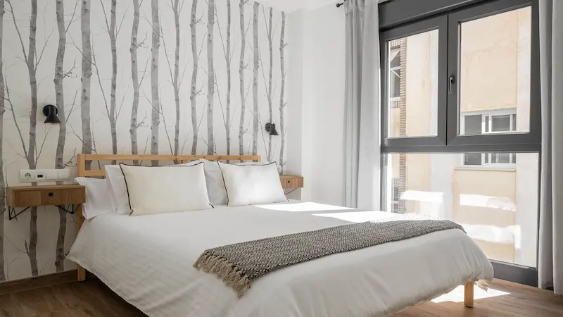 Habitación minimalista con ventana y cama de sábanas blancas.