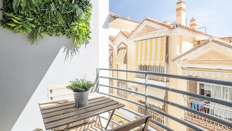 Balcón con mesa y planta, vistas a edificios con toldos amarillos y azotea.