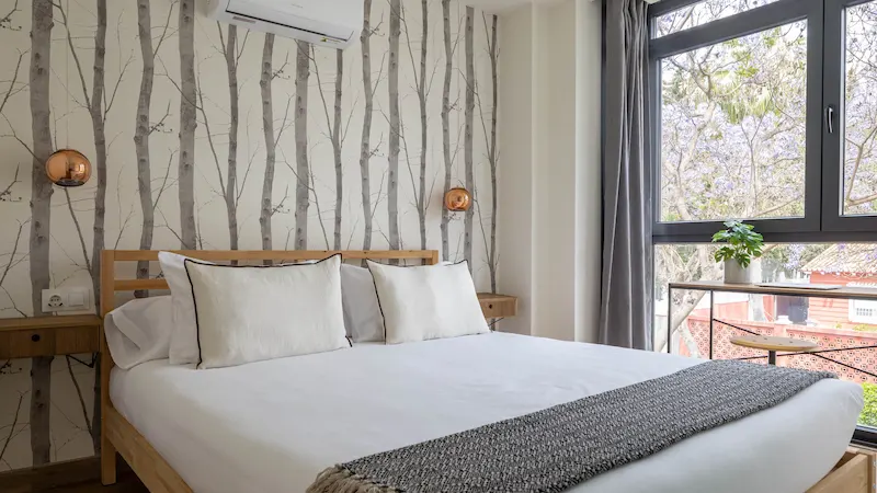 Habitación luminosa con cama blanca y ventana amplia.