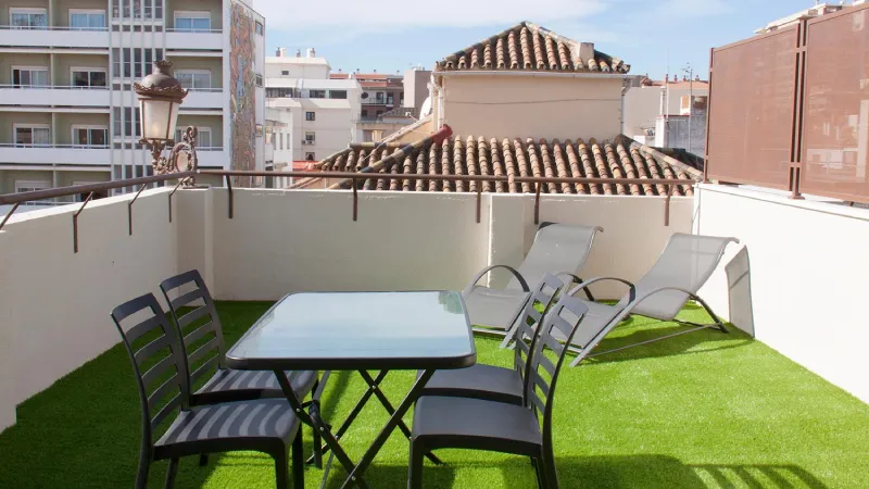 Terraza con césped artificial, mesa, sillas y tumbonas en una ciudad.