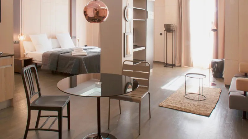 Habitación moderna con cama, mesa de comedor y luz natural.