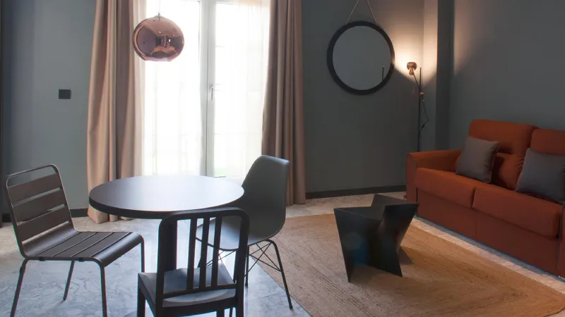 Sala moderna con sofá, mesas negras y luz suave filtrada por cortinas.