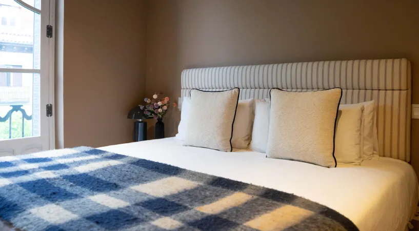 Habitaci&oacute;n moderna con cama doble y manta de cuadros, junto a ventana