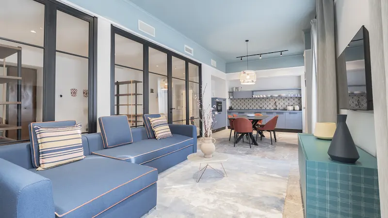 Sala moderna con sofá azul, cocina al fondo y decoración elegante en tonos azules y grises.
