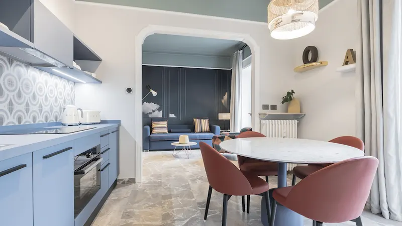 Cocina moderna con comedor y sala de estar al fondo, decorada en tonos azules y rosados.