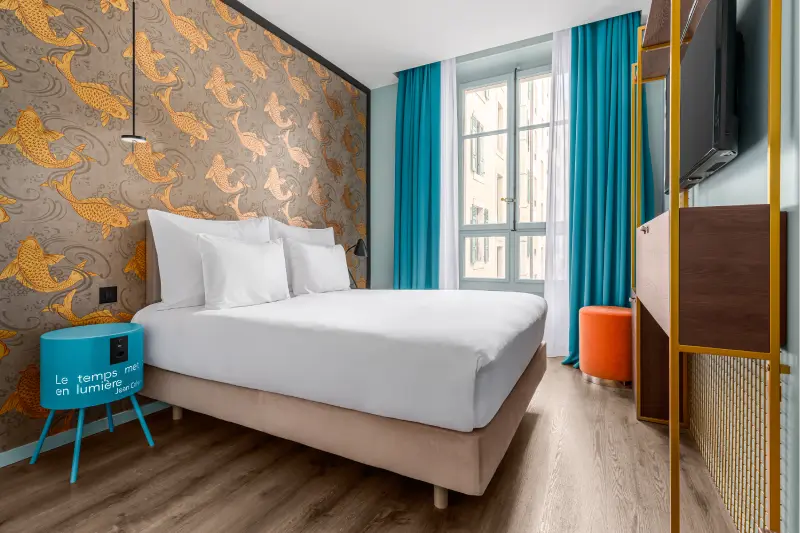 Chambre d'hôtel moderne avec tapisserie colorée, lit double, et rideaux bleus, vue sur la fenêtre.