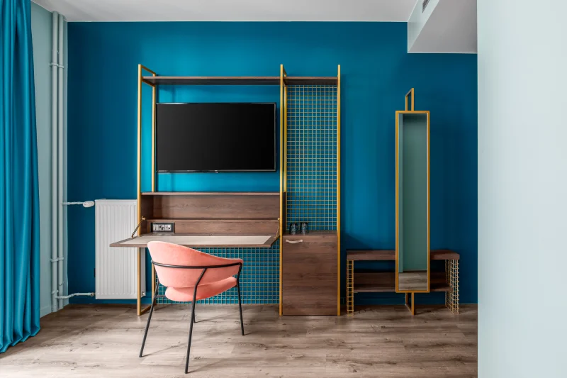 Bureau moderne avec chaise rose, meuble TV et miroir, sur mur bleu vif.