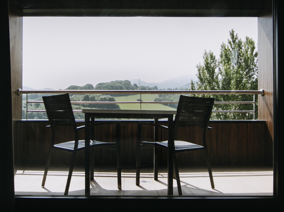 Dos sillas y una mesa en un balcón con vista a un paisaje verde y montañas al fondo.
