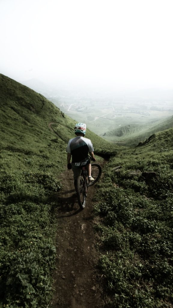Persona en bicicleta descendiendo por un sendero rodeado de colinas verdes cubiertas de niebla.