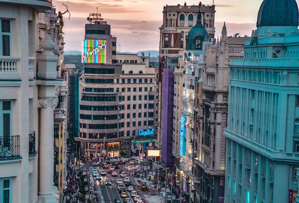 Calle concurrida al atardecer con edificios y anuncios luminosos, incluyendo "Schweppes".